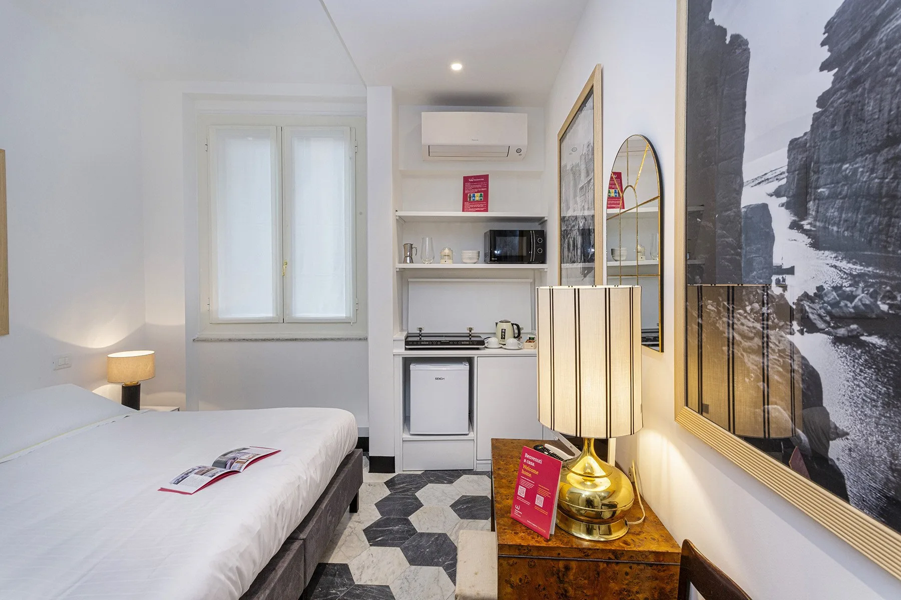 A bedroom with a bed, compact kitchenette, and a large wall photograph.