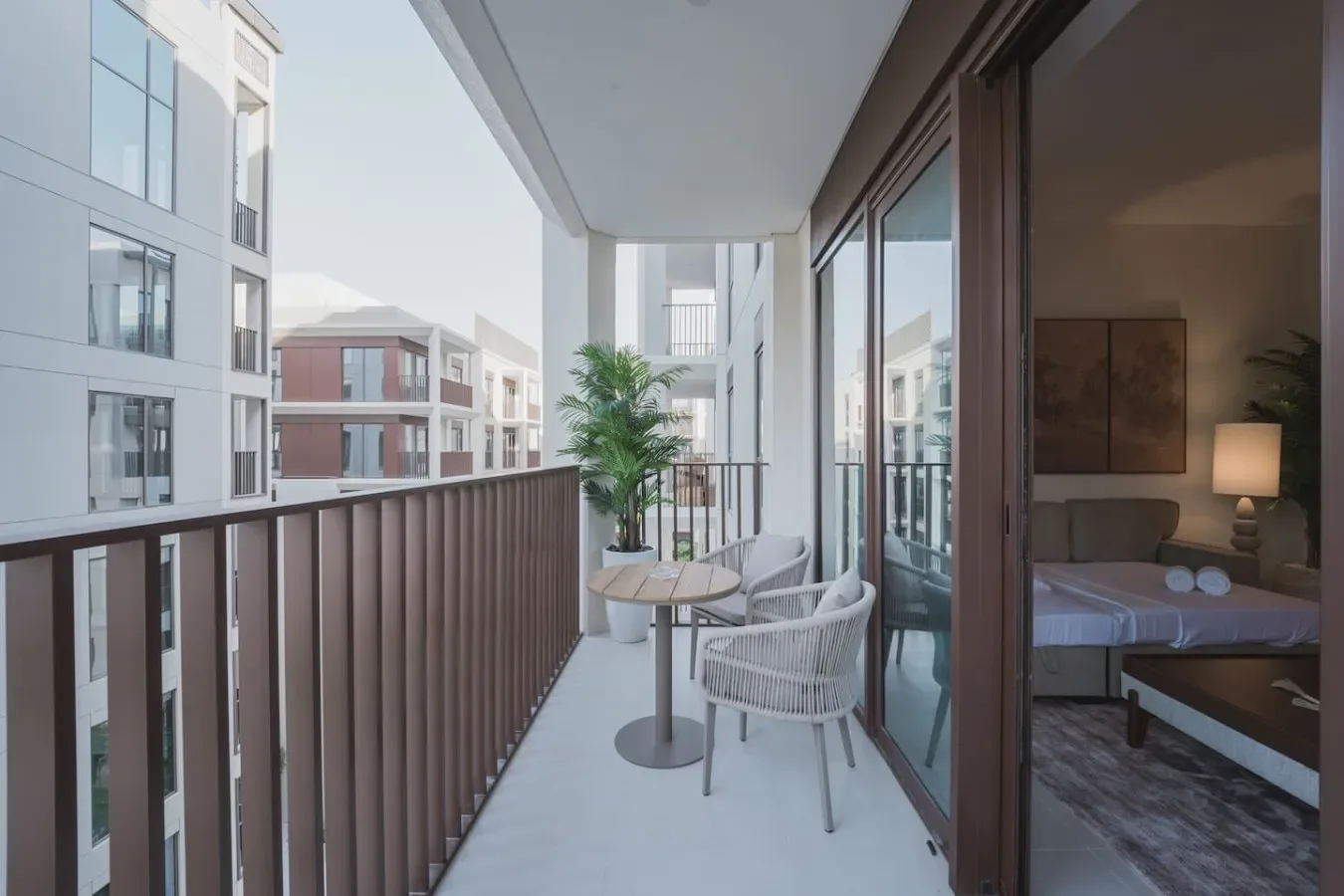 A balcony seating area overlooks neighboring buildings, with a bedroom visible through the open doorway.