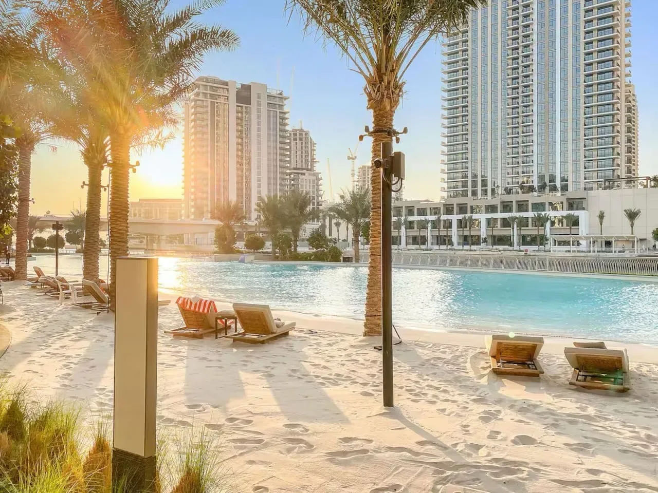 A poolside scene with lounge seating, palm trees, and high-rise buildings in the background.