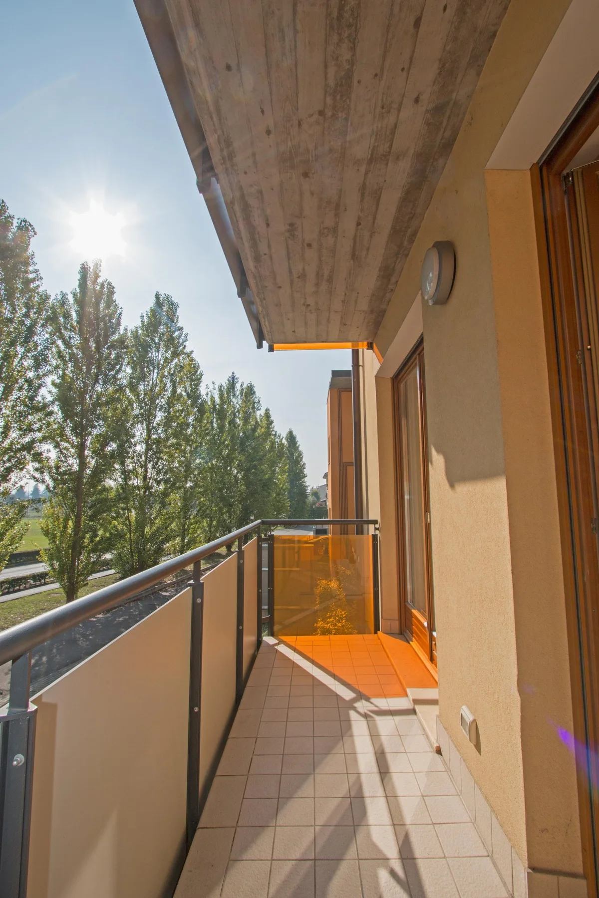 A narrow balcony with tiled flooring, a railing, and views of trees.