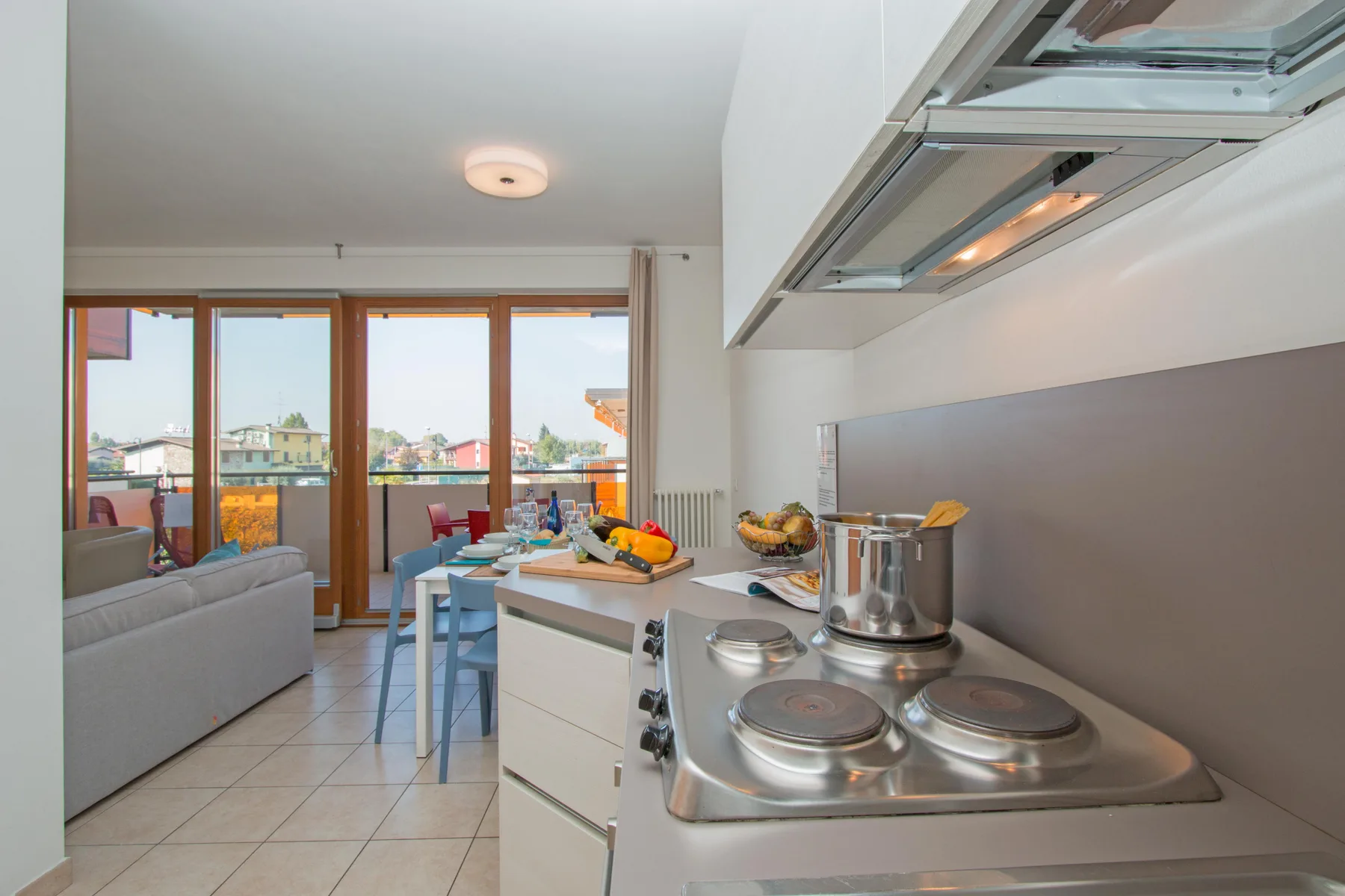 A kitchen with a stovetop and counter overlooks a dining area by large windows.