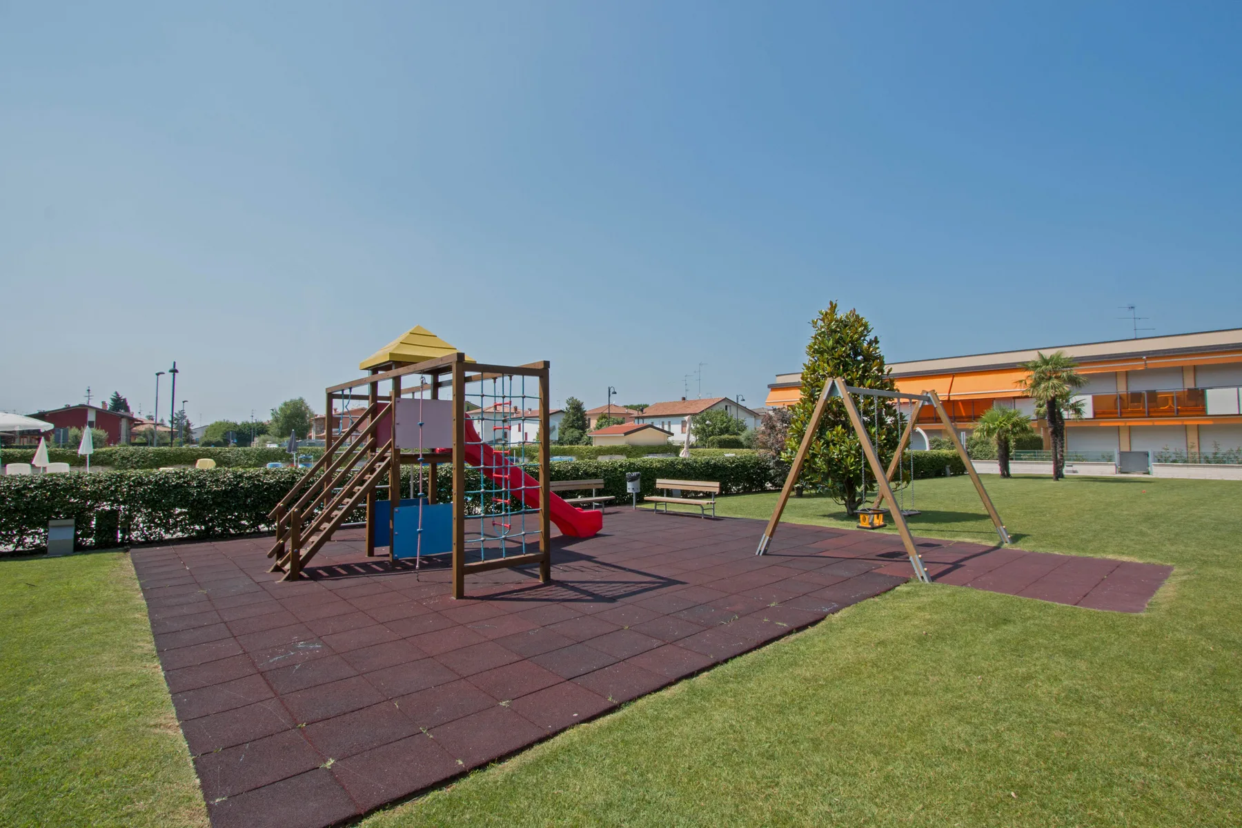 An outdoor playground with climbing equipment and swings on a paved play area.