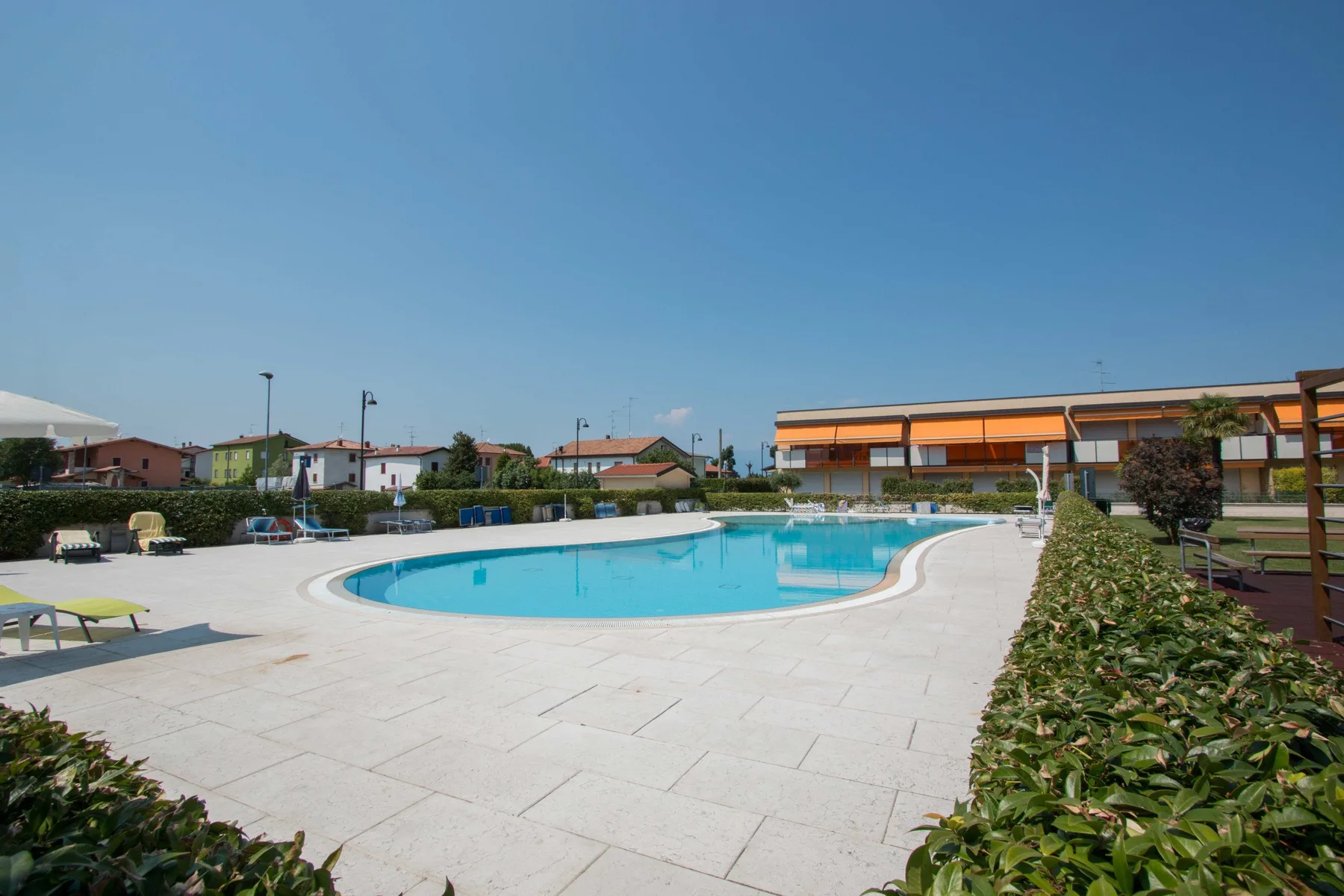 An outdoor swimming pool sits within a broad paved poolside area.
