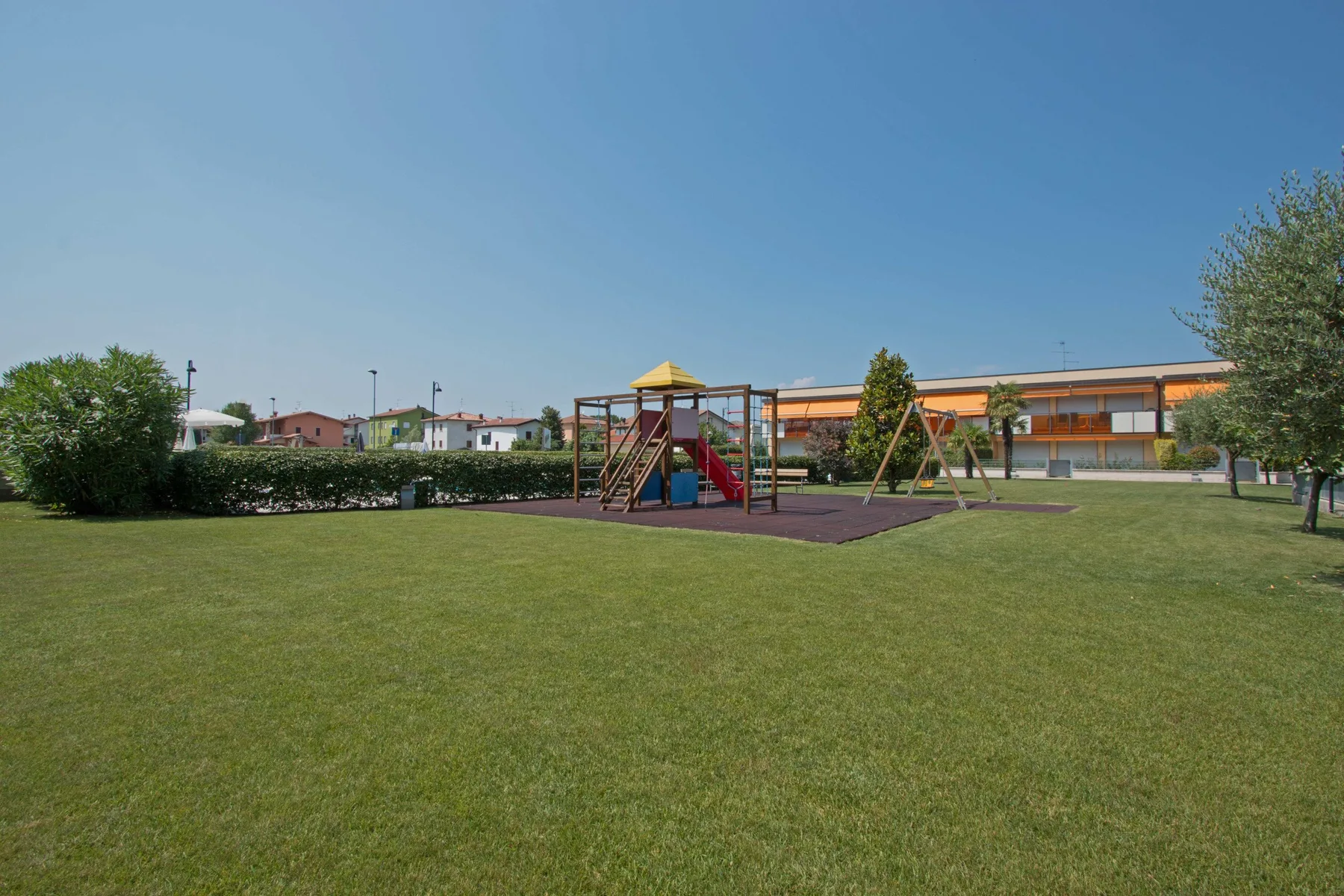 A playground with climbing equipment sits on a grassy lawn beside a low building.