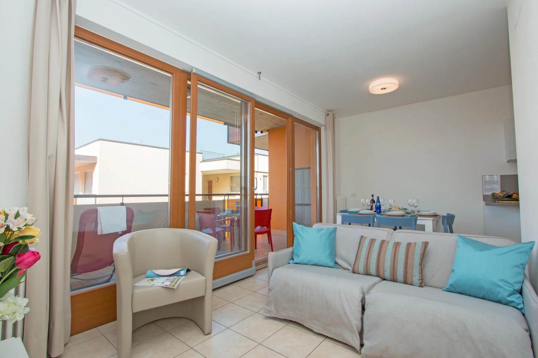 A bright living room with seating beside large windows and a dining table.