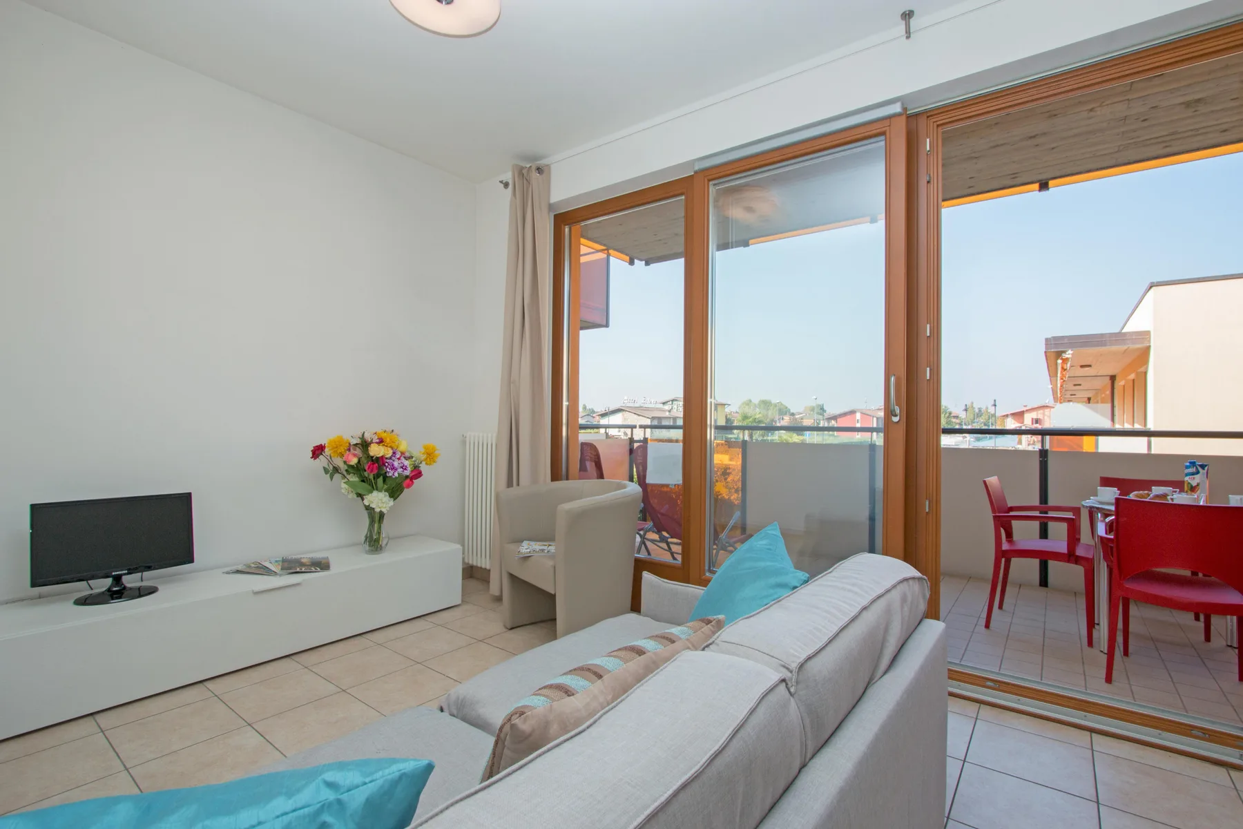 A bright living room opens onto a balcony through large glass doors.