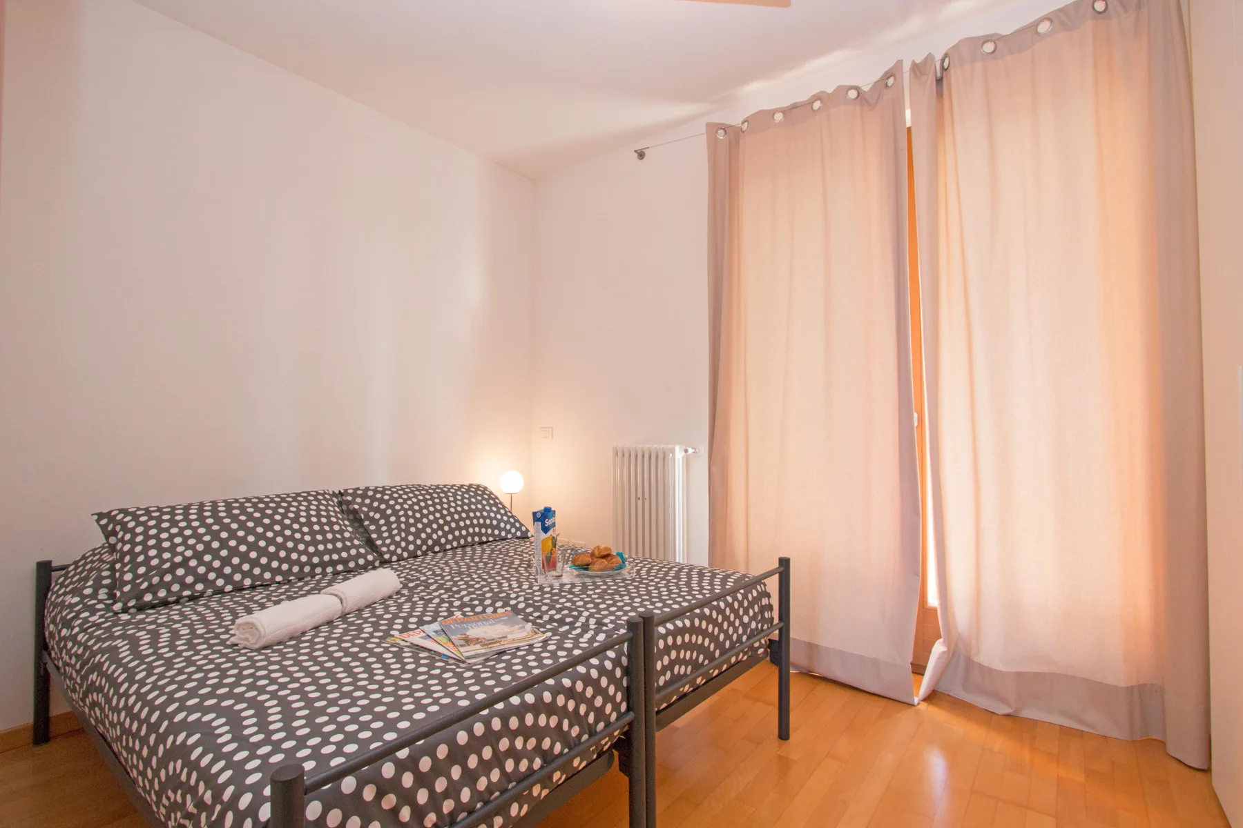 A bedroom with patterned bedding and pale curtains over the windows.