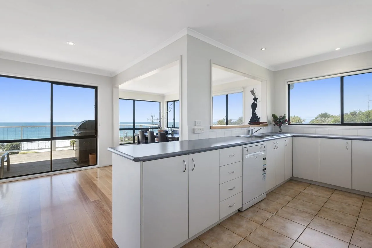 Una cocina luminosa con una encimera central y grandes ventanas con vistas al océano.