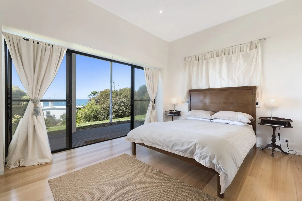 Un dormitorio luminoso con una cama grande junto a puertas corredizas de vidrio con vista al océano.