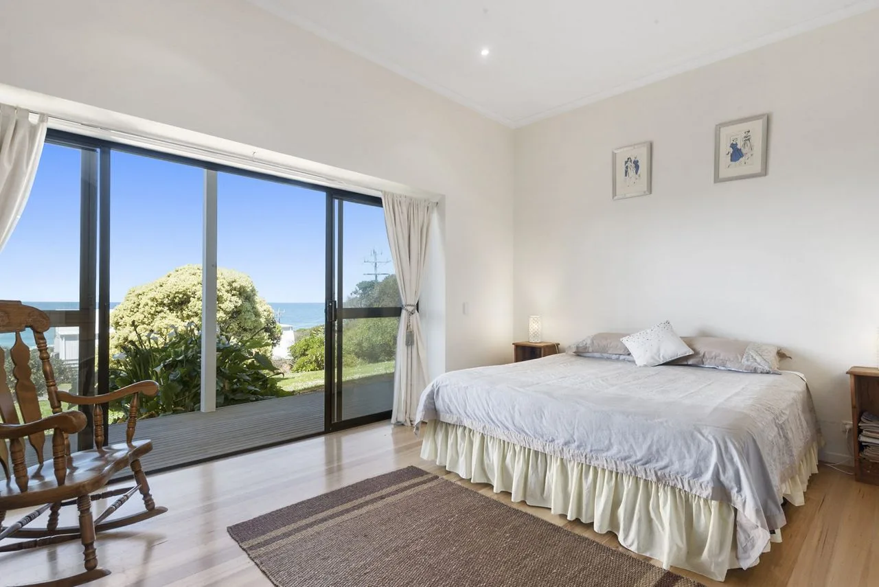 Un dormitorio luminoso con una cama grande junto a puertas de vidrio con vistas al mar.