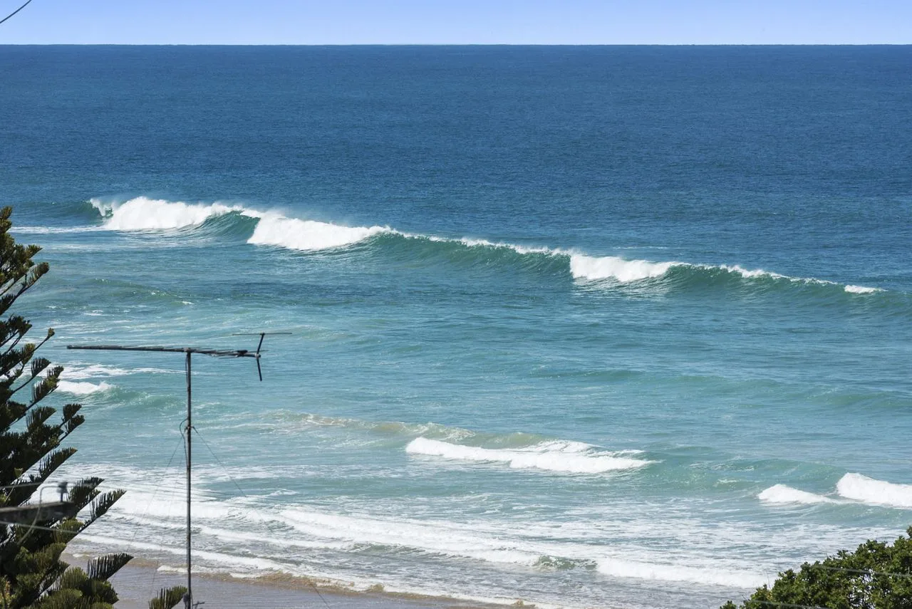 Las olas del océano llegan a una playa arenosa bajo un cielo despejado.