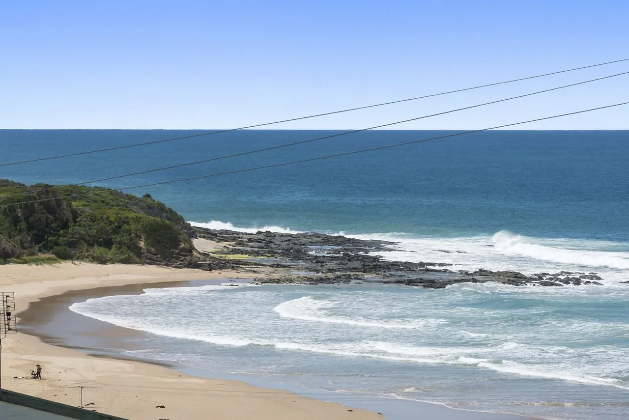 Una playa de arena bordea el océano, con costa rocosa y vegetación baja.