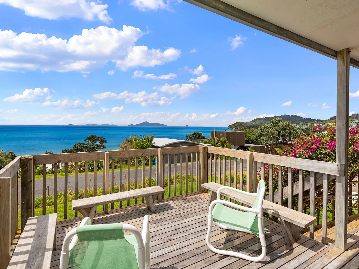 A wooden deck with two green chairs and built-in benches overlooking the ocean and surrounding landscape at Bay View Bach - Langs Beach