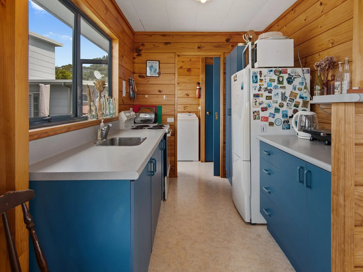 Una cocina con armarios azules, encimeras blancas y paredes de madera en Bay View Bach Langs Beach