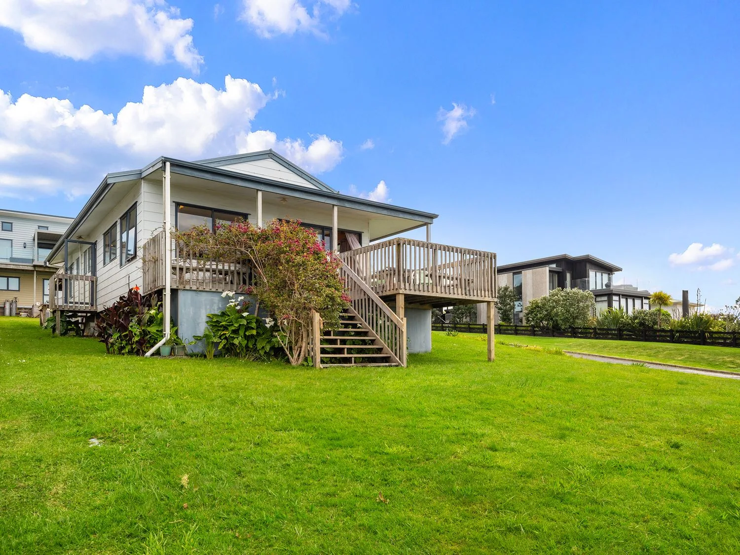 A single story house with a wooden deck and stairs surrounded by grass at Bay View Bach - Langs Beach Holiday Home in Langs Beach