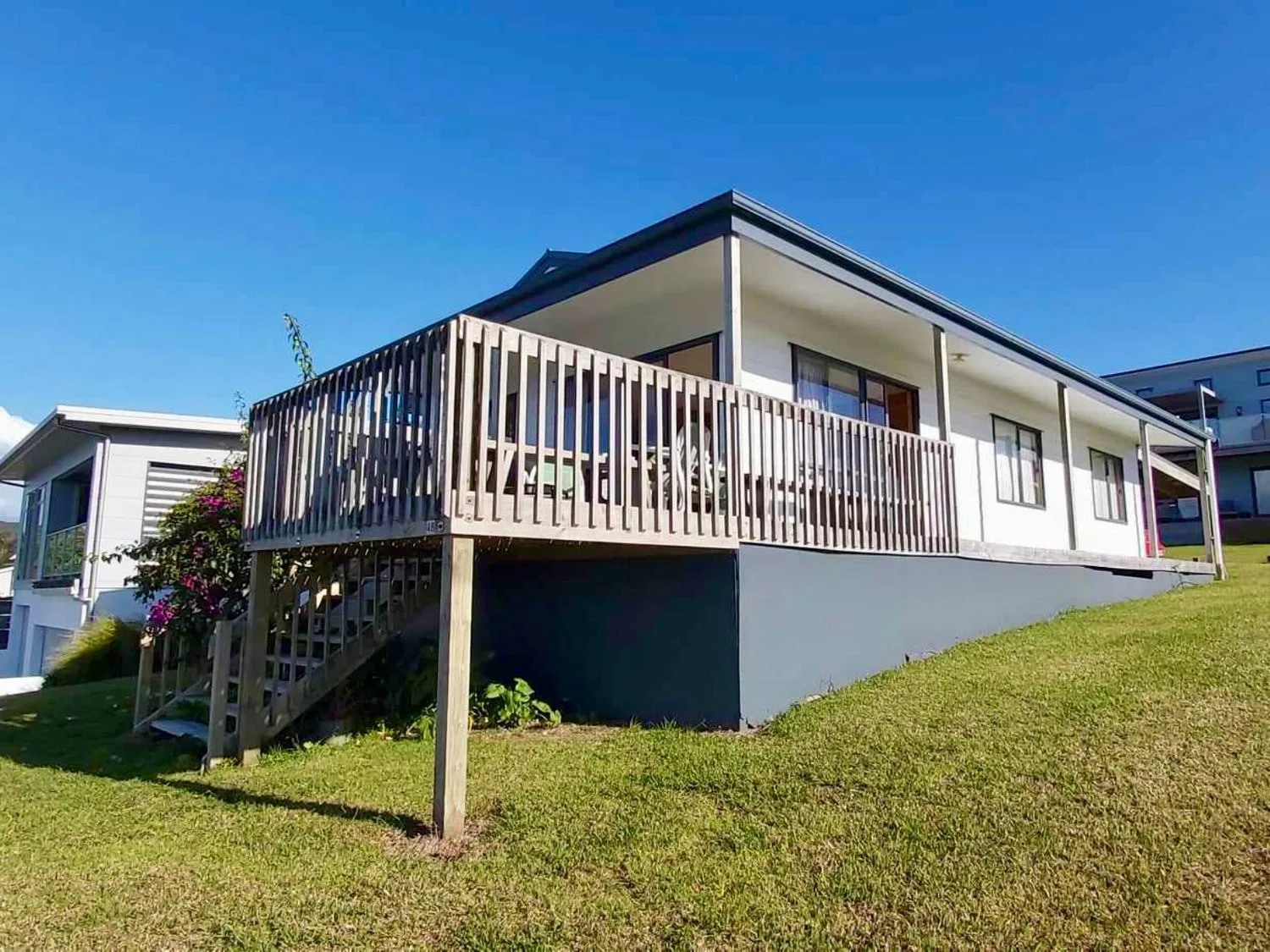 Una casa de una sola planta con una terraza de madera y escaleras sobre un terreno con césped en Bay View Bach - Langs Beach Holiday Home, en Langs Beach