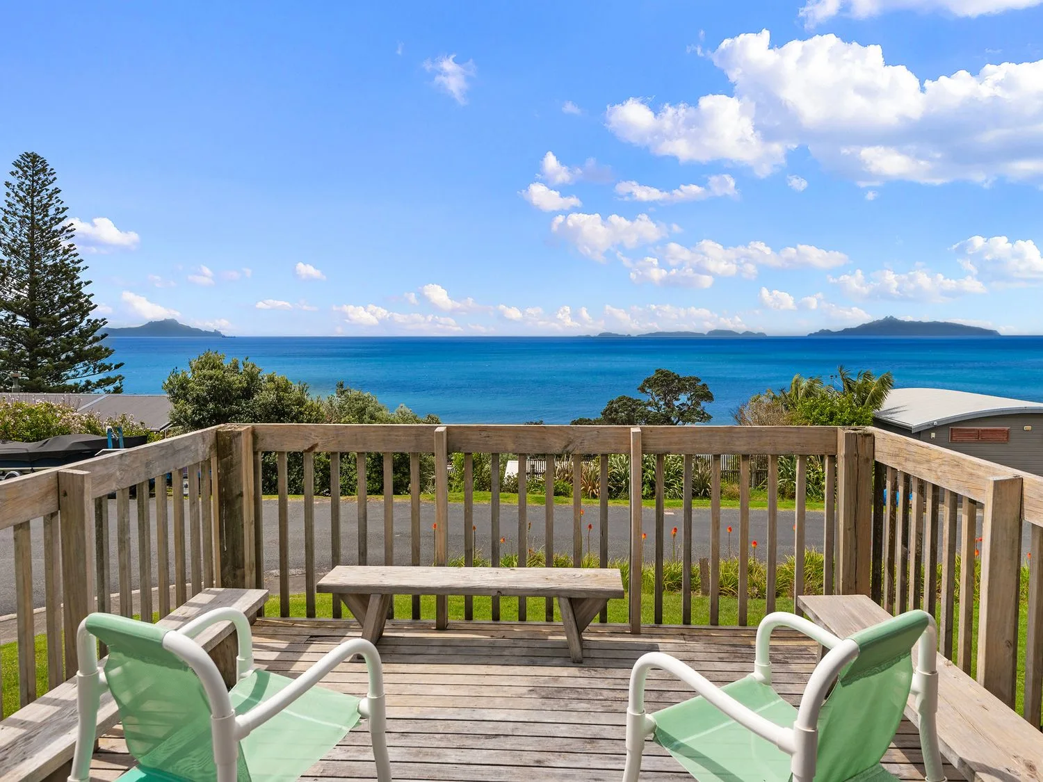 A wooden deck with two green chairs and a bench overlooking the ocean and islands at Bay View Bach Langs Beach