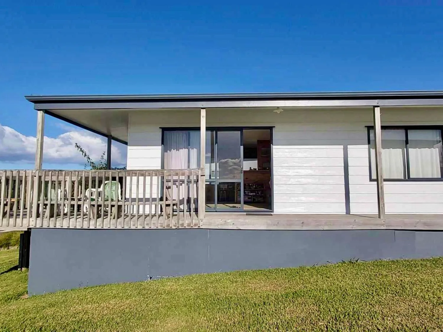 Una casa con una terraza de madera y sillas sobre el césped en Bay View Bach - Langs Beach Holiday Home, en Langs Beach