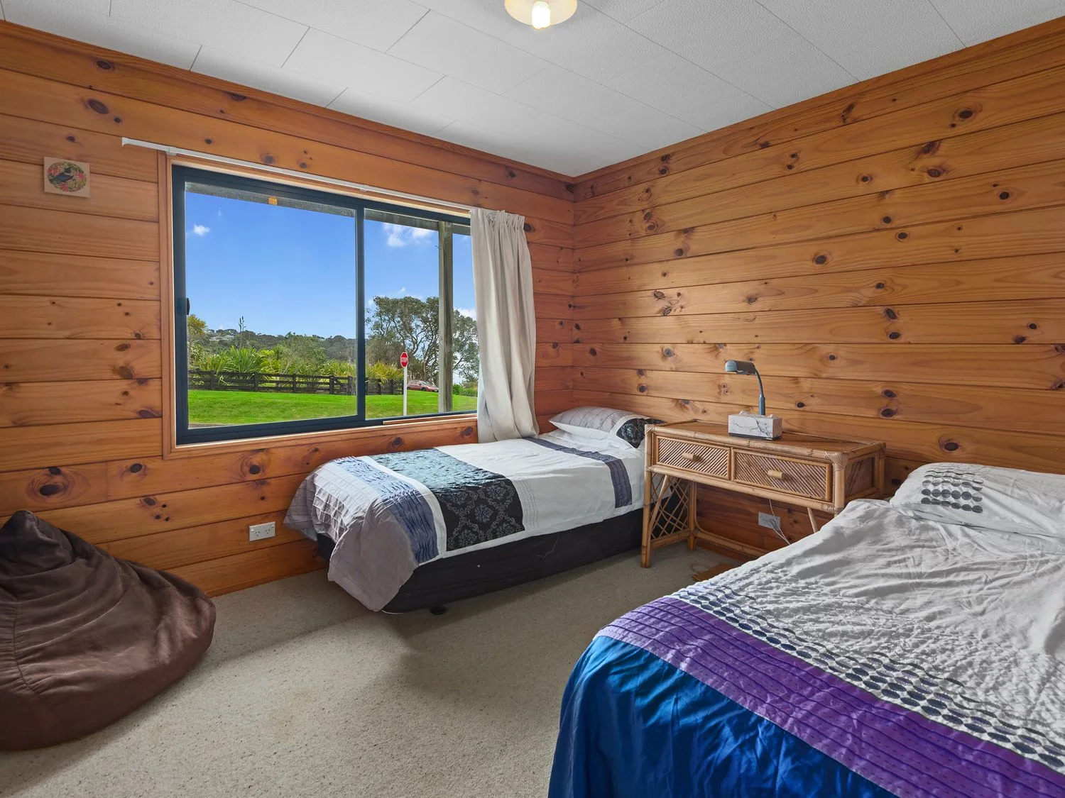 Un dormitorio con dos camas individuales, un puf marrón y una pequeña mesa de madera entre las camas en Bay View Bach Langs Beach