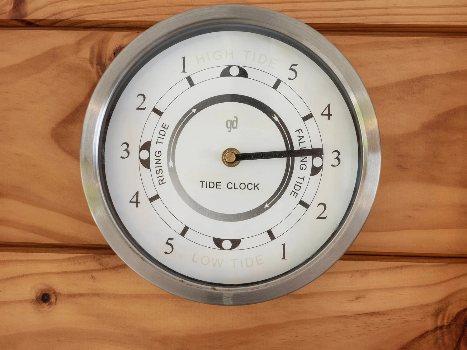 A tide clock hangs on a wooden wall, with rising and falling tide markings.