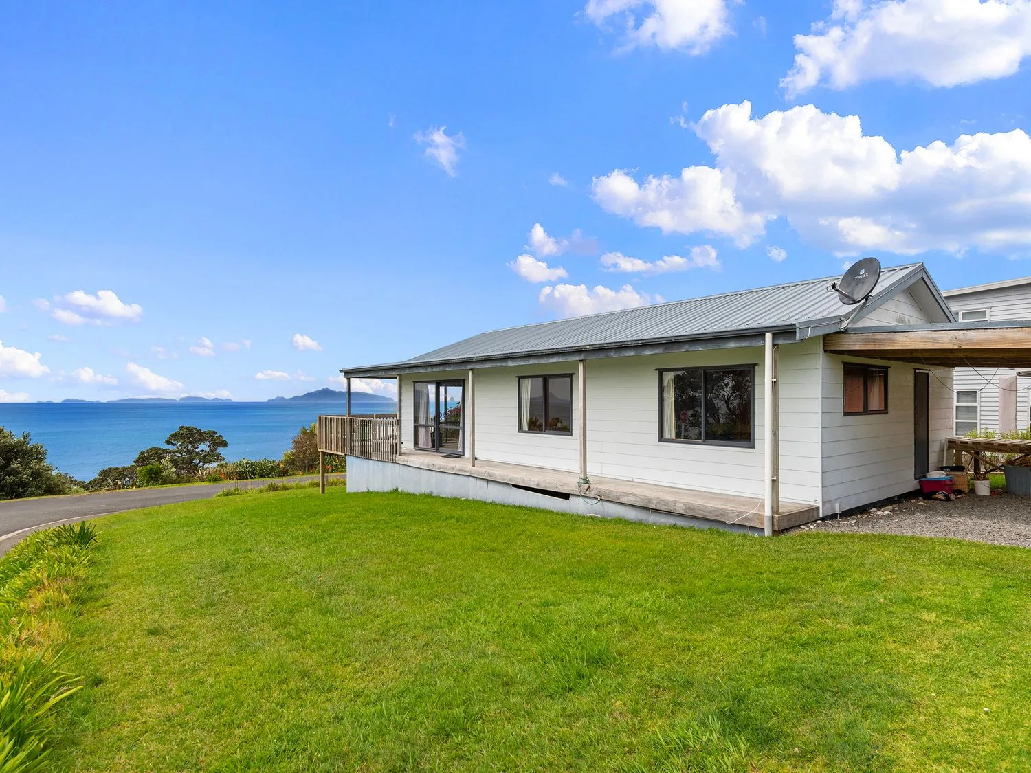 A white house with a metal roof on a grassy lawn near the ocean at Bay View Bach Langs Beach