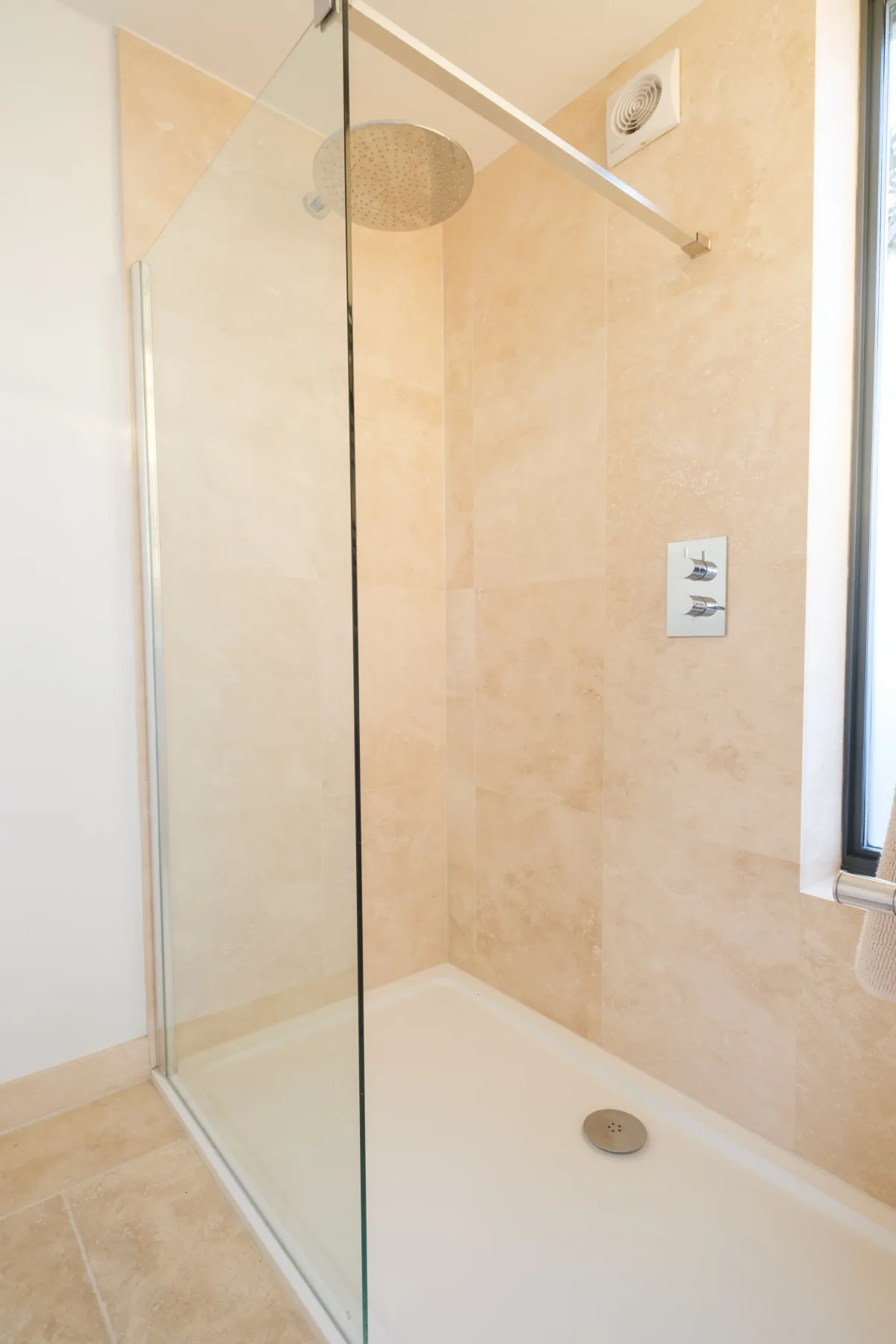 Una ducha con azulejos, un panel de vidrio y un cabezal de ducha en la pared.