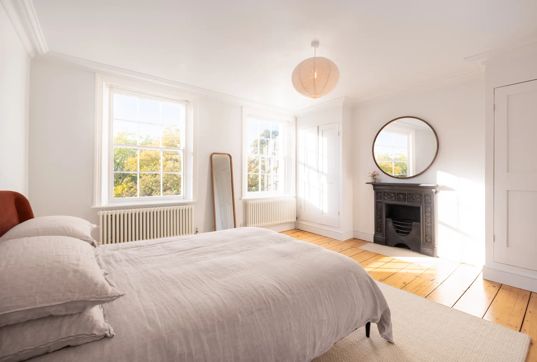A bright bedroom with a bed, tall windows, and a fireplace.