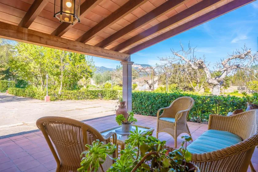 A covered outdoor patio with wicker seating and plants overlooks a garden.
