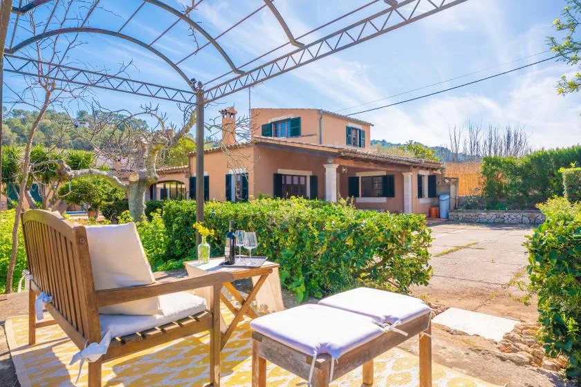 An outdoor patio with cushioned seating overlooks a garden and a house.