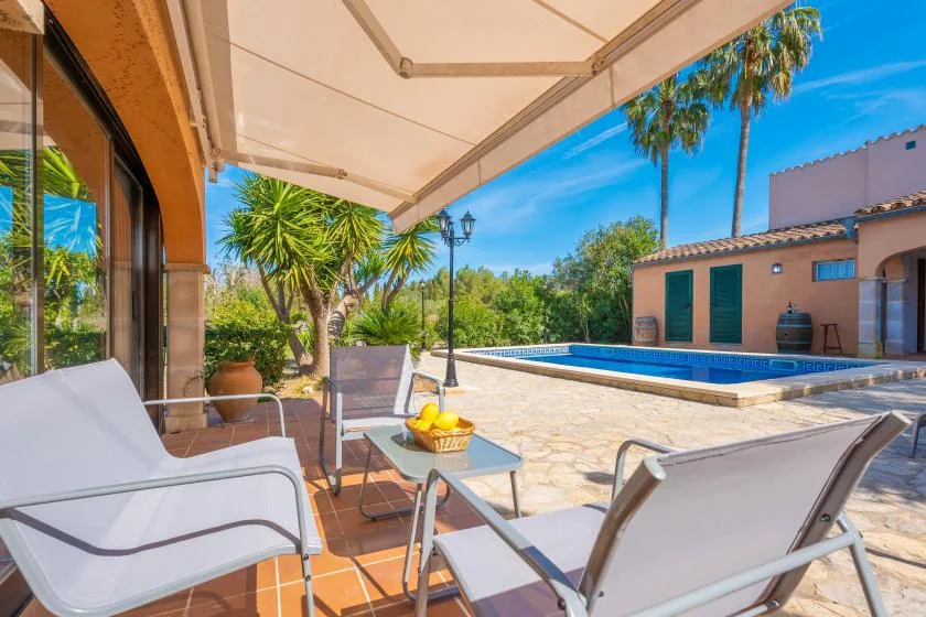 A covered patio with outdoor seating overlooks a swimming pool and garden.
