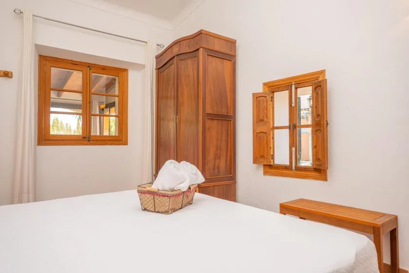 A bedroom with a bed, a wooden wardrobe, and two windows.