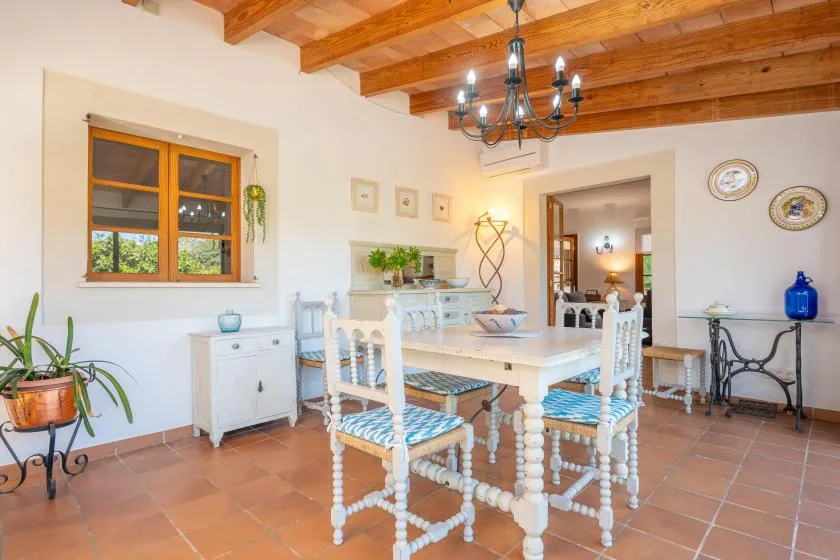 A dining room with a white table and chairs beneath exposed wooden ceiling beams.
