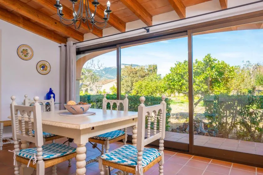 A dining area with a table and chairs beside large glass windows overlooking greenery.