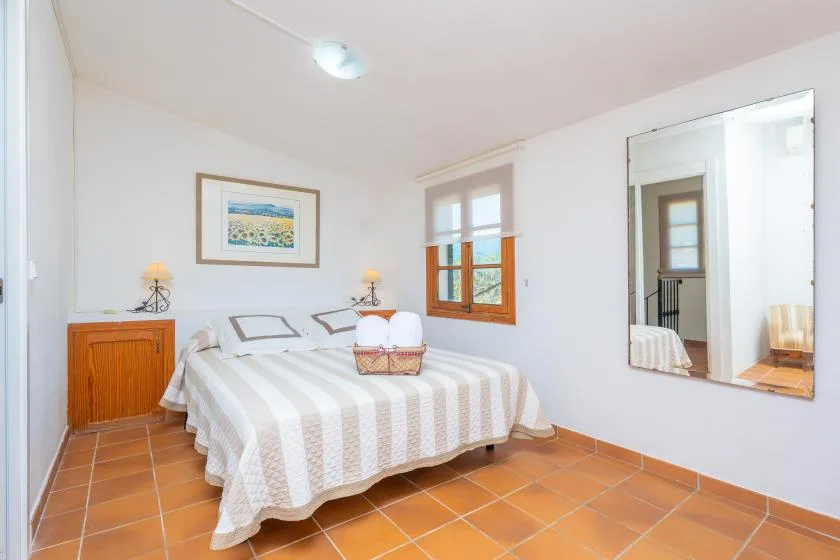A bedroom with a striped bedspread, wooden window, and tiled floor.