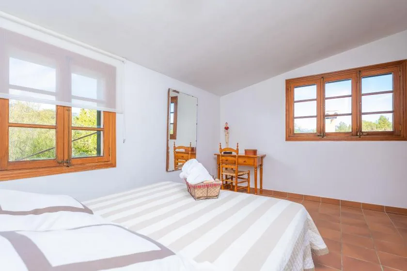 A bedroom with a striped bedspread, wooden windows, and a small table.