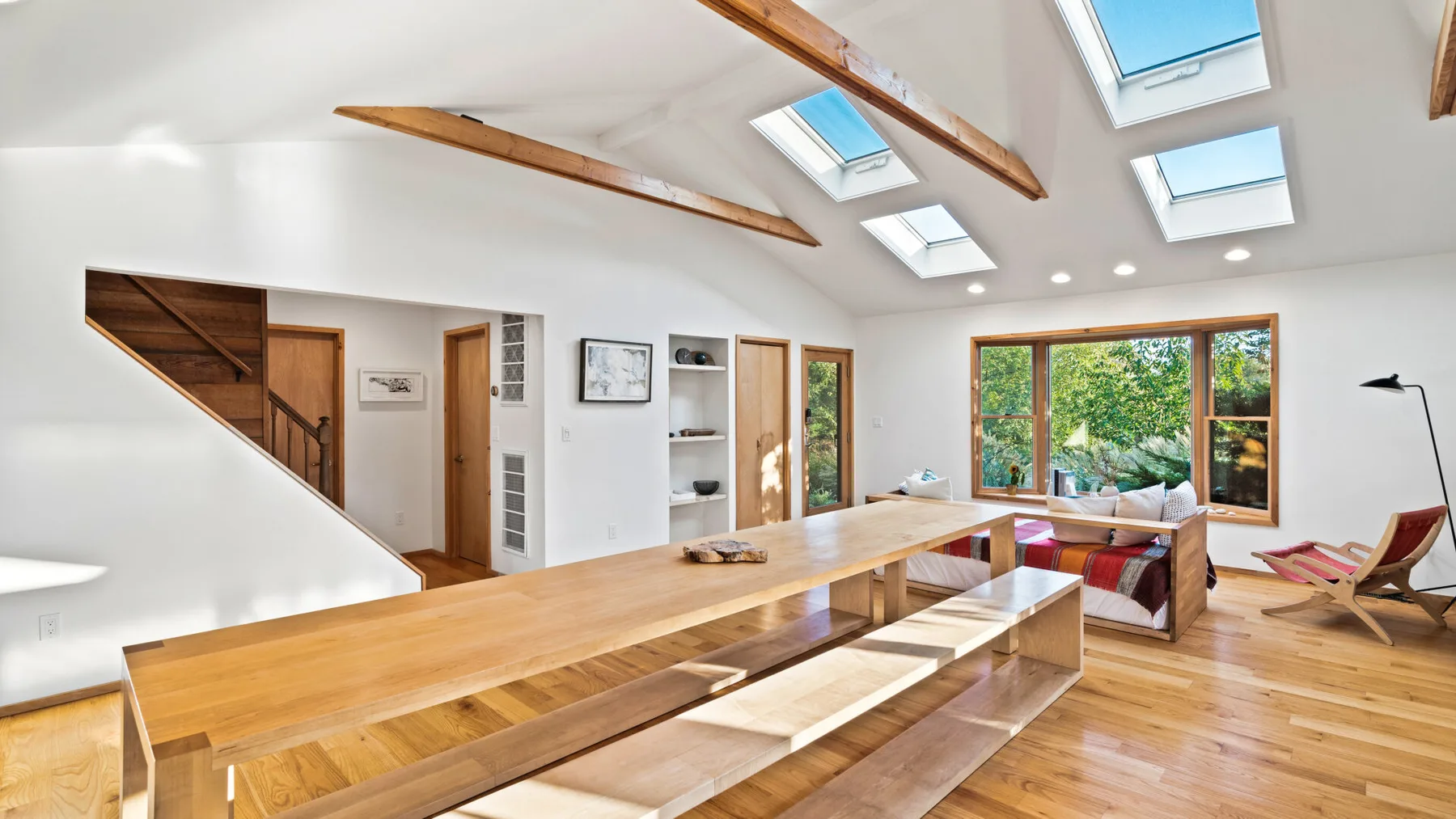 Una luminosa sala de estar abierta con una mesa larga de madera y ventanas grandes.