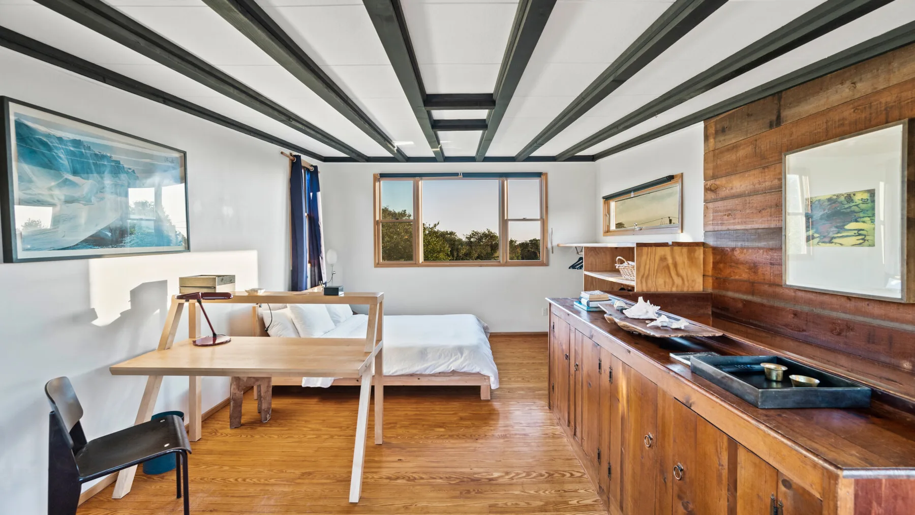 Un dormitorio y una pequeña cocina comparten una habitación luminosa con armarios de madera y una cama.