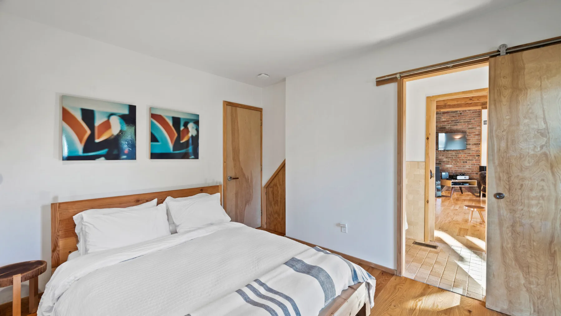 Un dormitorio luminoso con una cama de madera y cuadros coloridos en la pared.