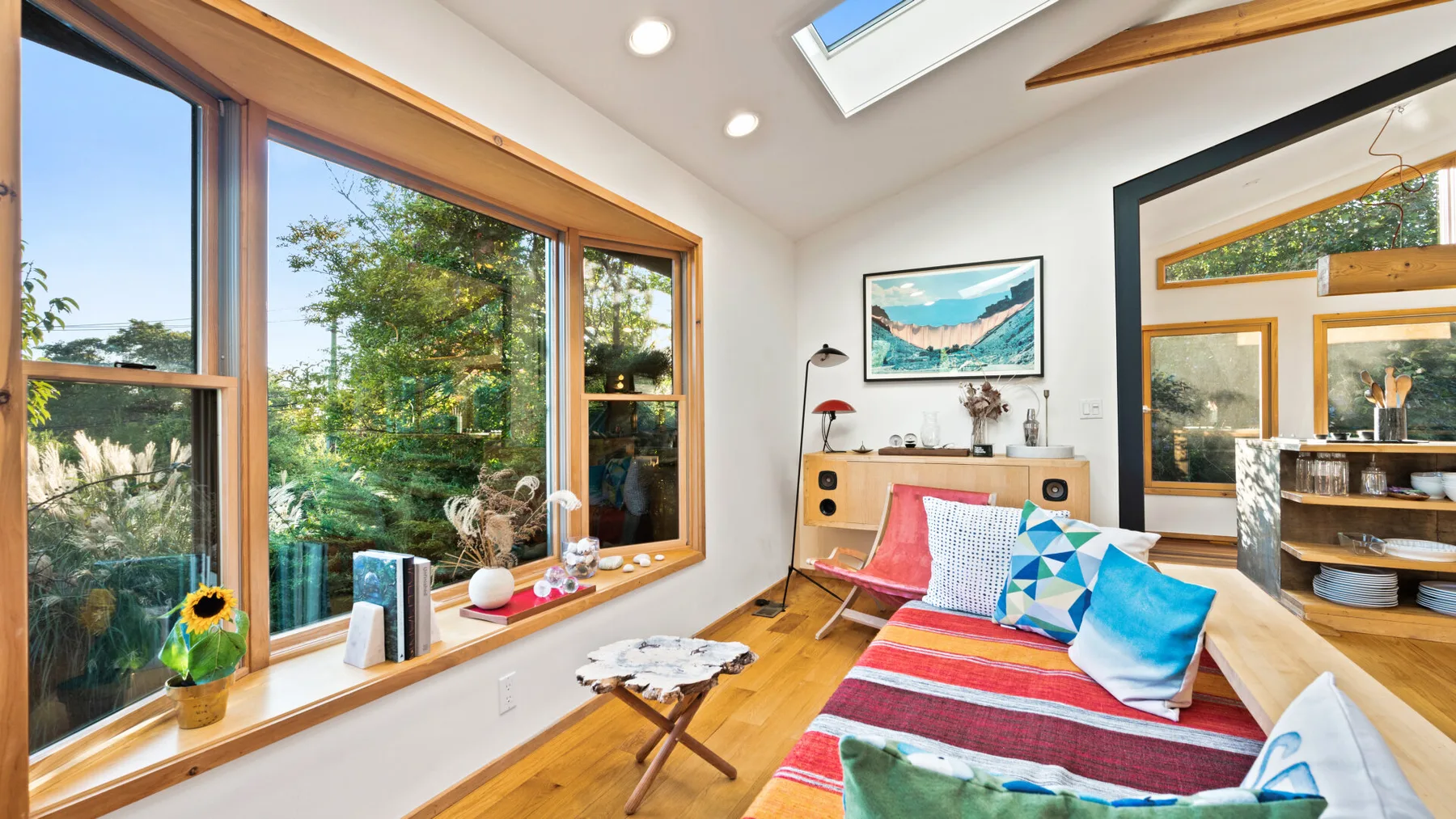 A bright living room with colorful seating beside large windows overlooking greenery.