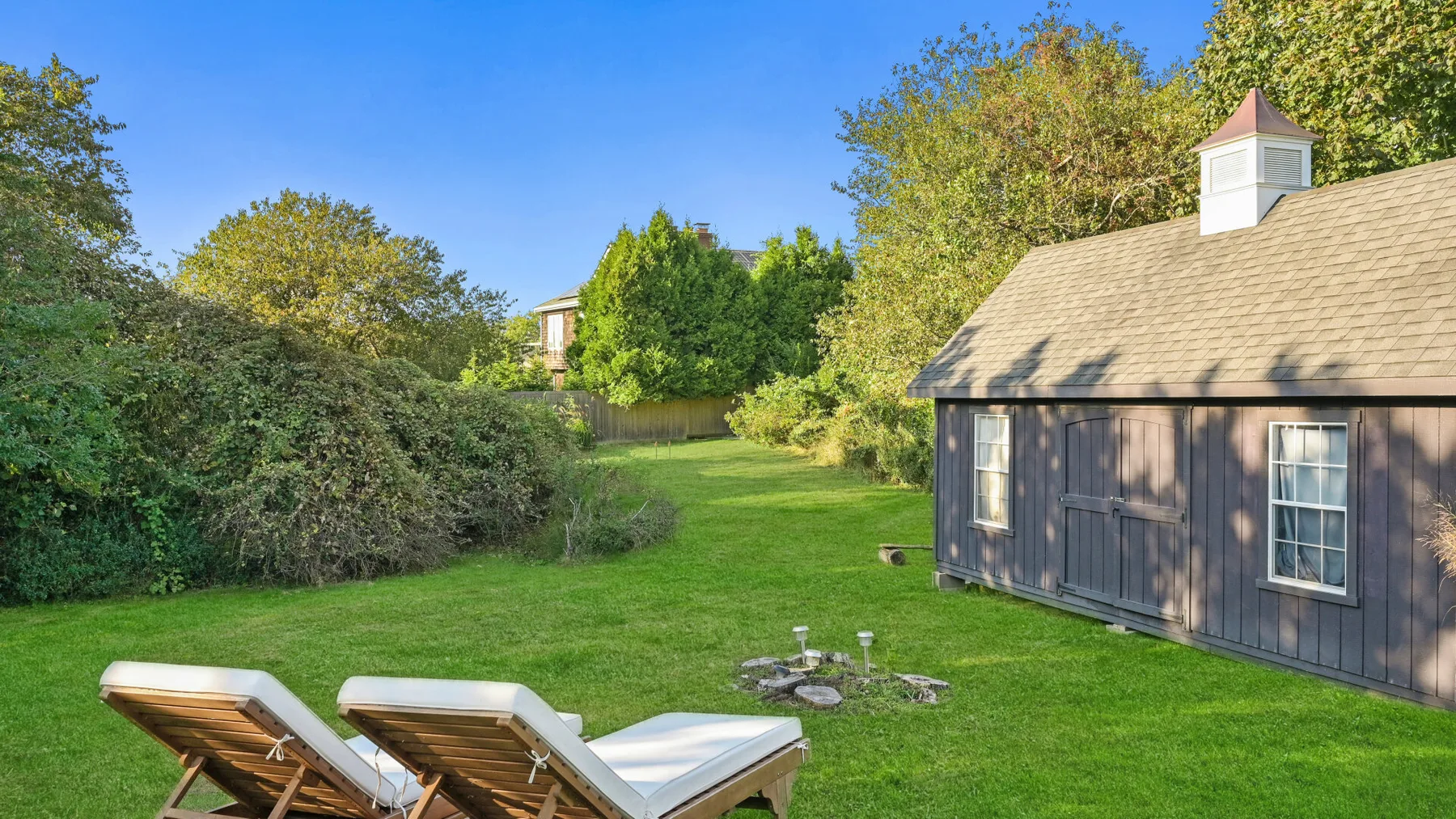 A grassy backyard with lounge seating and a small shed beside the lawn.