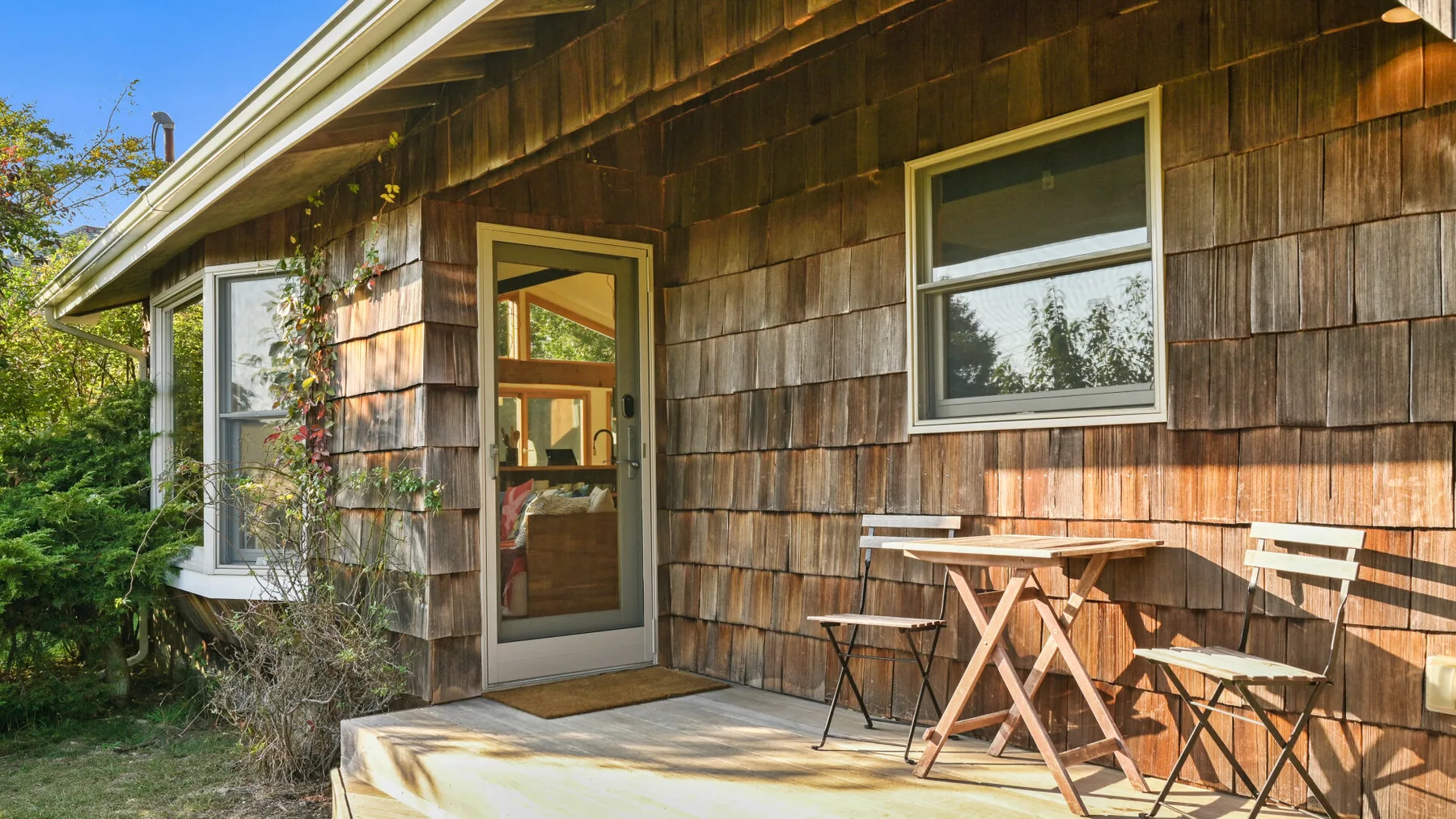 Exterior de una casa de madera con un pequeño patio y asientos al aire libre.