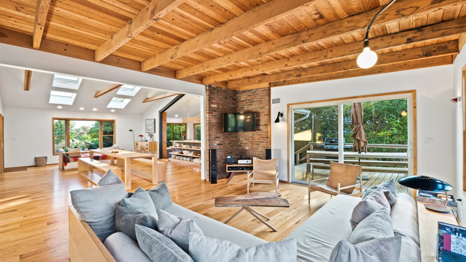 A bright living room with gray seating and large windows overlooking greenery.