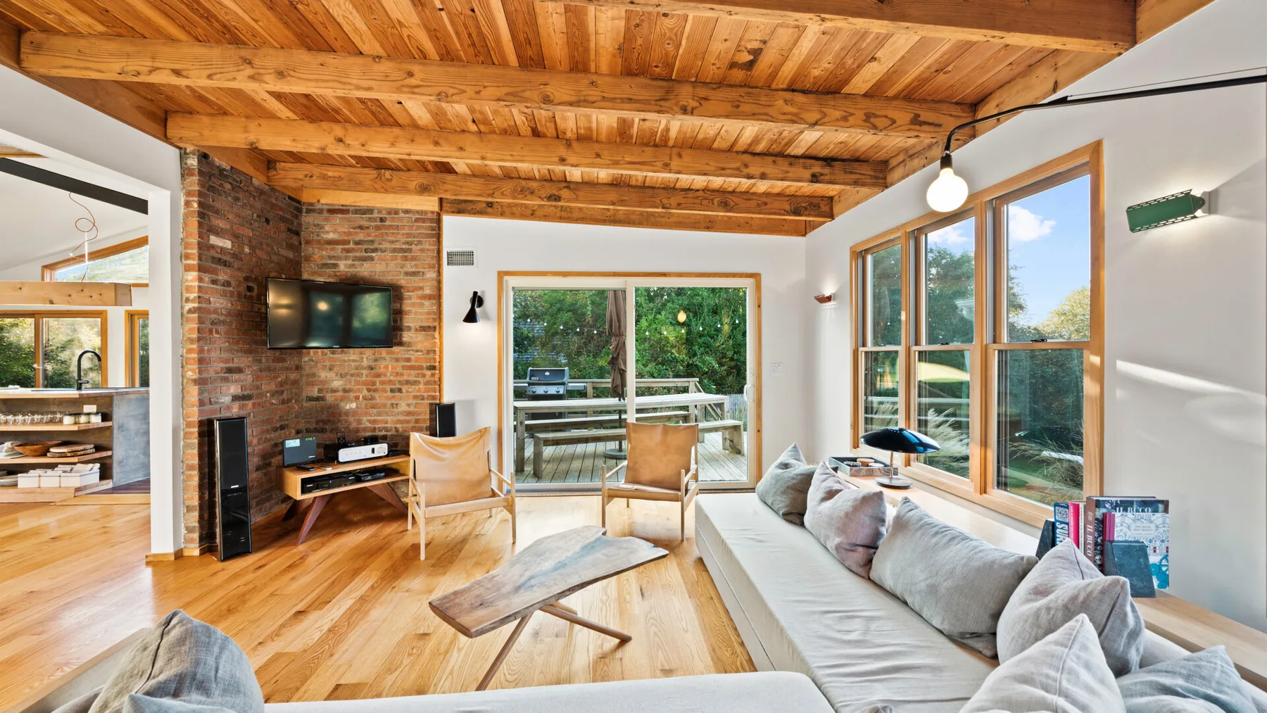 Una sala luminosa con asientos, un televisor y grandes ventanas.