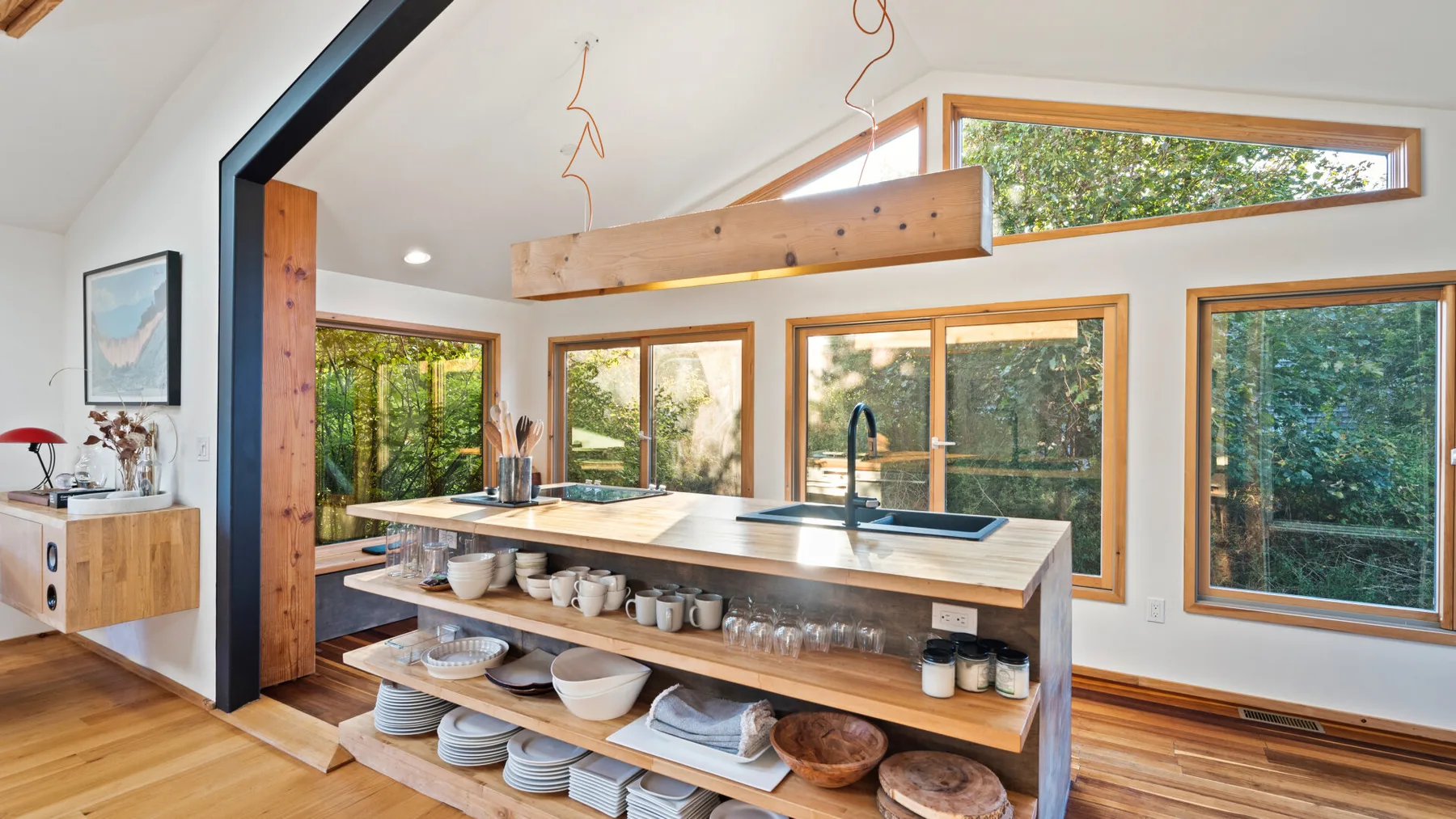 Una cocina luminosa con una isla larga, estantes abiertos y ventanas grandes.