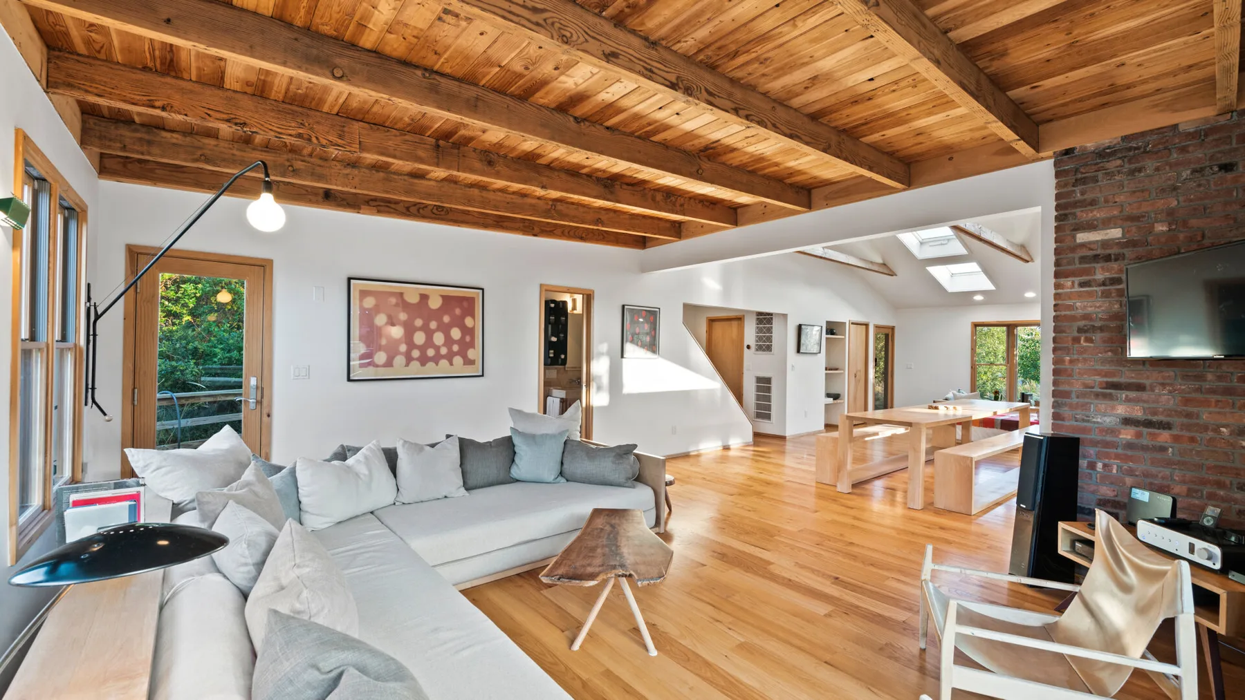 Una sala de estar luminosa y abierta, con asientos claros y vigas de madera a la vista.