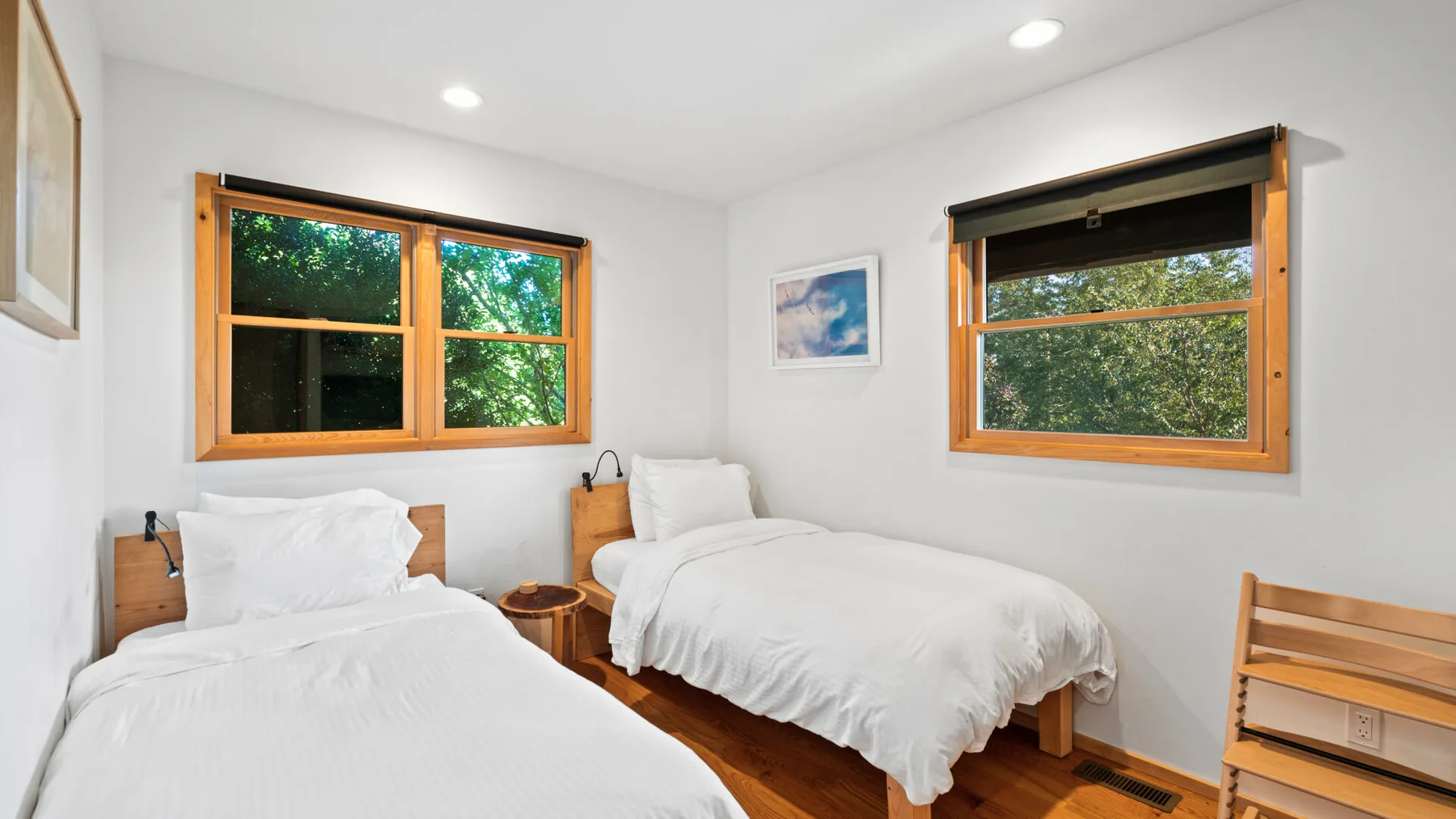 Un dormitorio luminoso con dos camas junto a ventanas con marcos de madera.