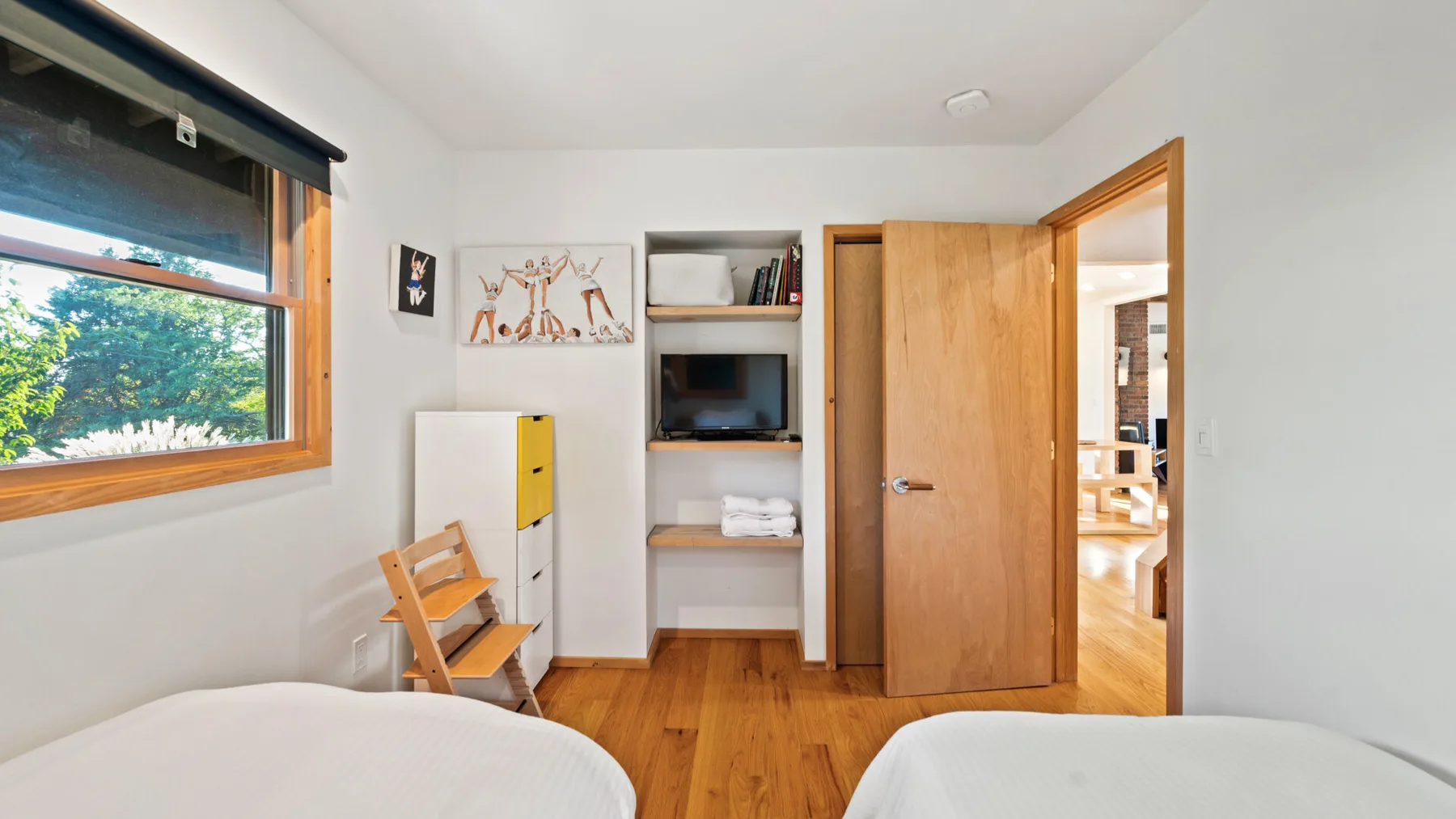 Un dormitorio luminoso con dos camas, suelo de madera y estanterías empotradas.