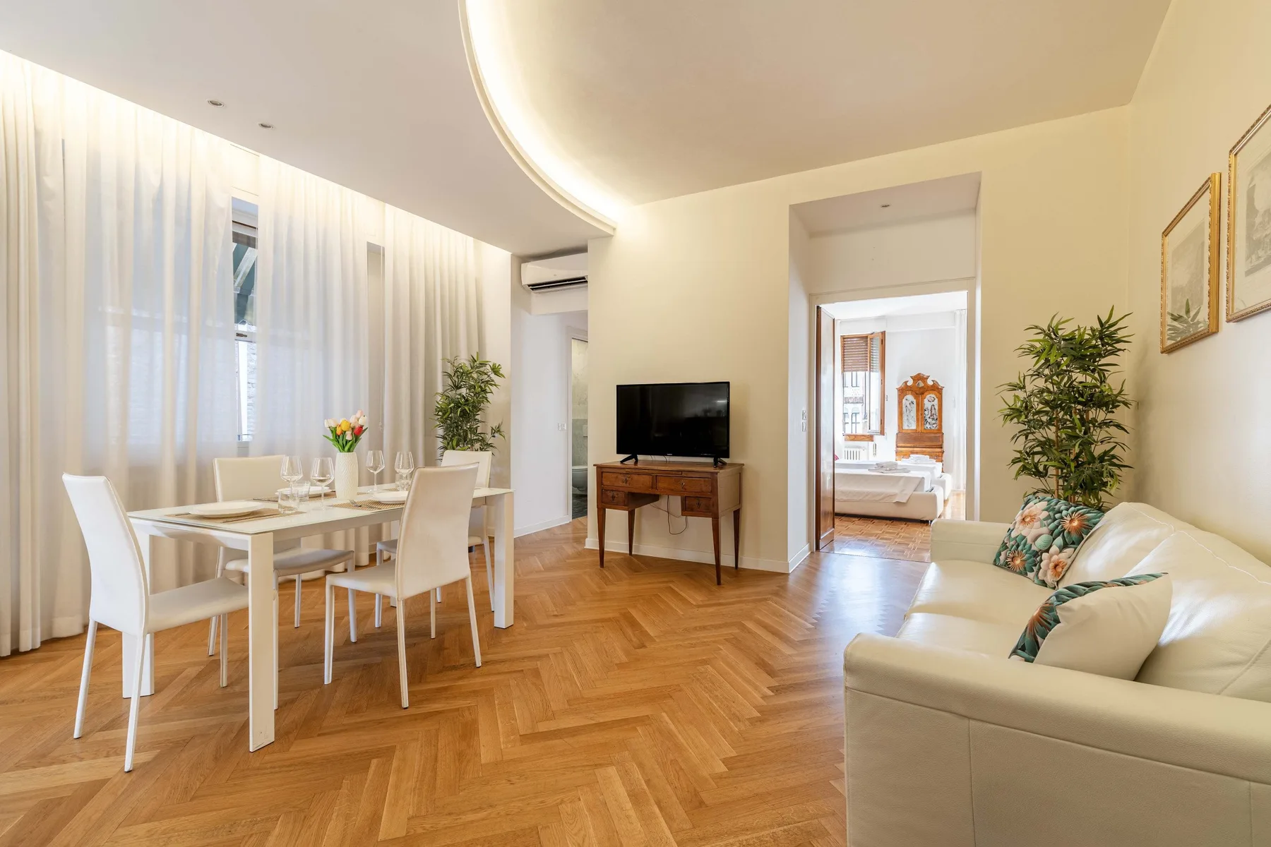 Una luminosa sala de estar y comedor con televisor y asientos de tonos claros.