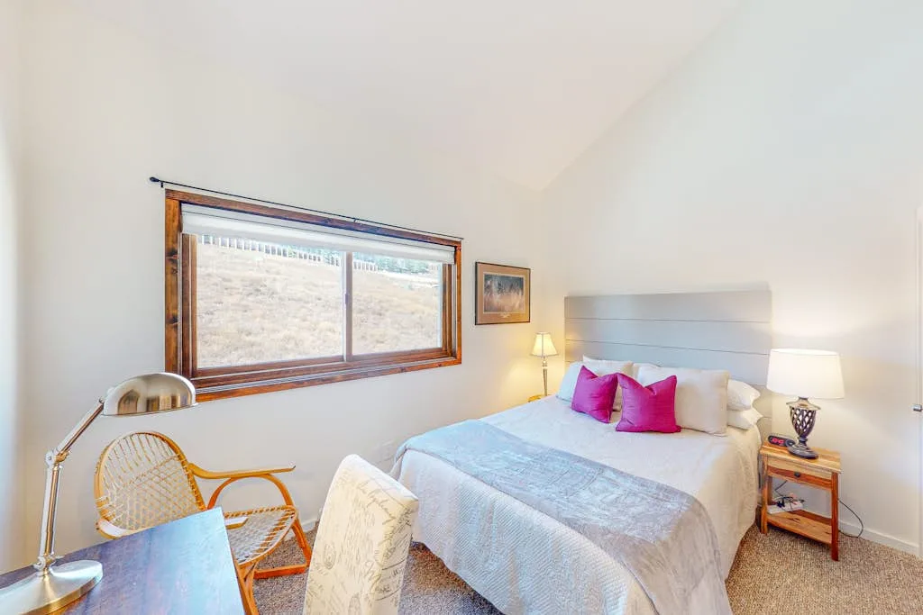 A bright bedroom with a neatly made bed and a large window.