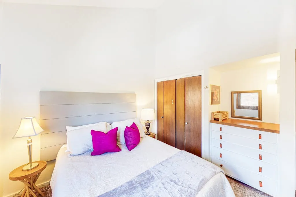 A bright bedroom with a bed beside a wooden wardrobe and white dresser.